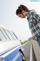 A woman leaning against a blue and white van on the side of the road.