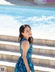 A woman in a blue dress standing by a swimming pool.