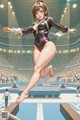 A woman in a black leotard jumping over a balance beam.