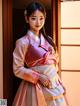 A woman in a pink and white hanbok standing in front of a window.