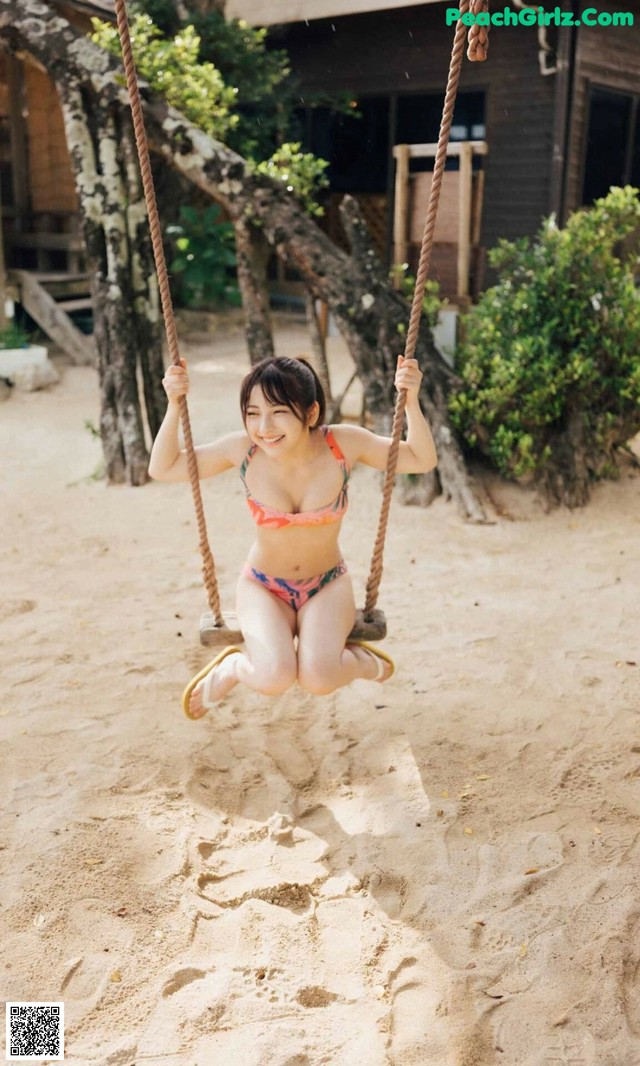 A woman in a bikini swinging on a swing.